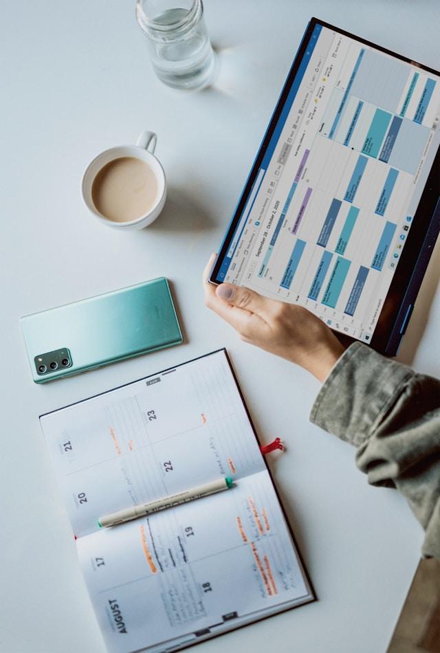 A weekly schedule open on a laptop beside a paper planner